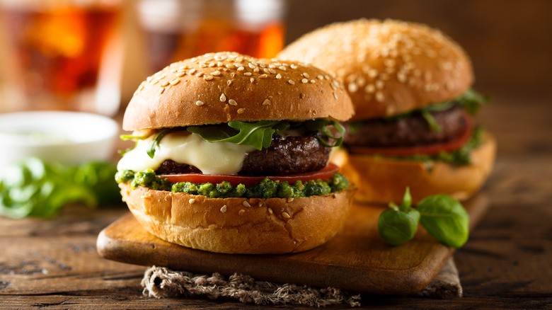 Caprese burgers with beef patty, mozzarella, arugula, pesto, tomato, and basil on the side.