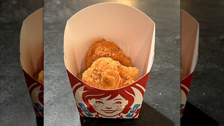 A box of Wendy's chicken nuggets featuring the red white and blue Wendy's logo with several crispy nuggets inside sitting on a dark table top