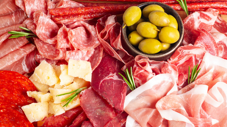 Close-up of a charcuterie board with meats, cheeses, olives, and herbs