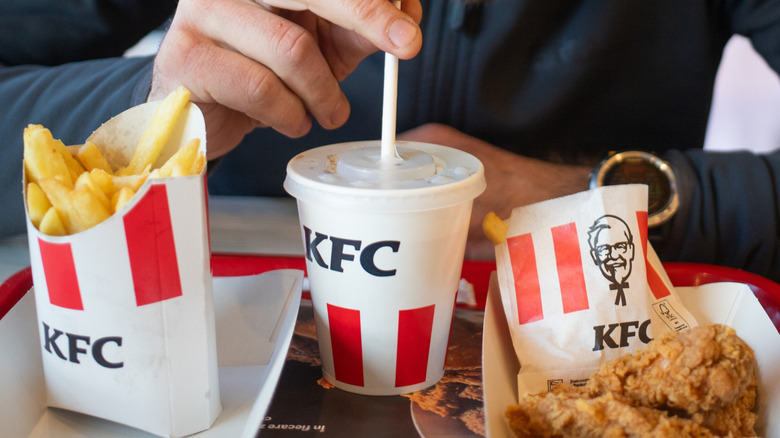A person with a KFC combo that includes french fries in a box, small drink, and some fried chicken