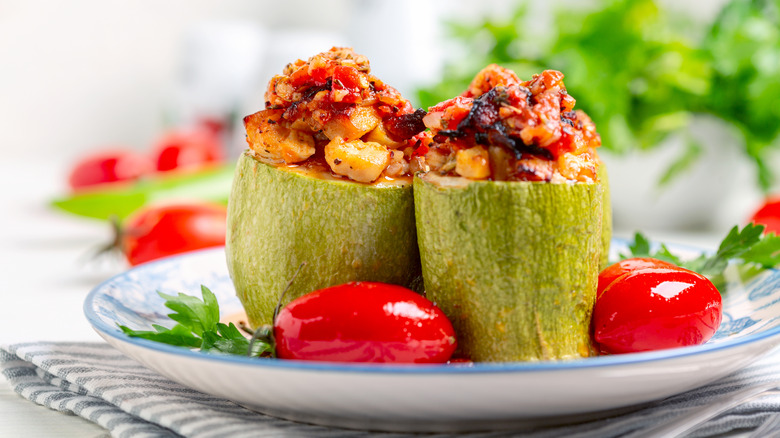 two stuffed zucchini cylinders on a white plate with fresh grape tomatoes