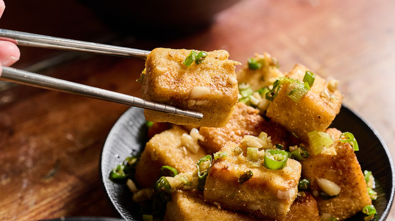 chopsticks lifting tofu off of plate