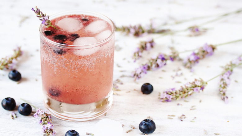 A blueberry lemonade cocktail in a glass garnished with lavender sprigs and fresh blueberries