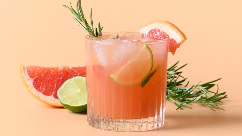 A pink Greyhound cocktail garnished with lemon and grapefruit wedges and rosemary