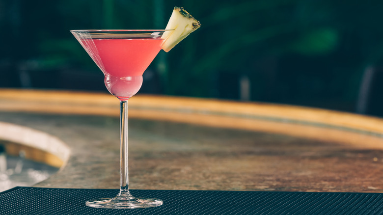 A martini glass containing a cranberry pineapple cocktail garnished with a wedge of pineapple