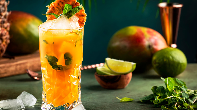 A mango cocktail in a highball glass, garnished with a slice of mango and basil leaves