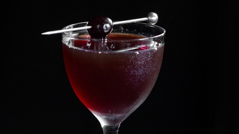 A black cherry cocktail in a glass garnished with a cherry