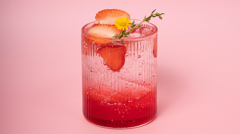 A short glass with a pink liquid inside, garnished with strawberry and rosemary