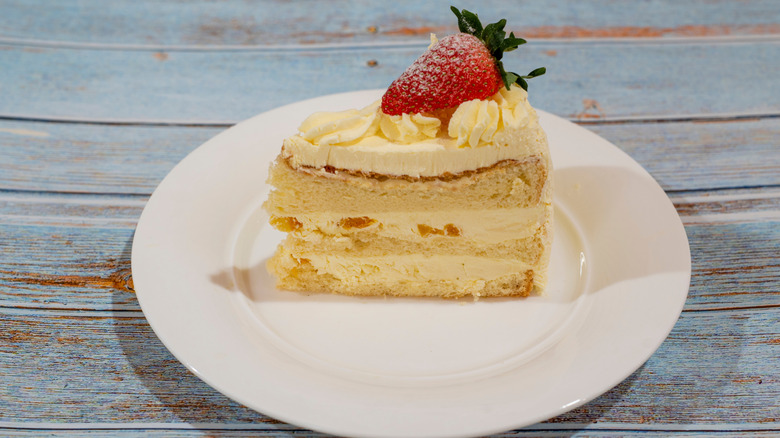 Fruit cream cake slice on a white plate with a strawberry