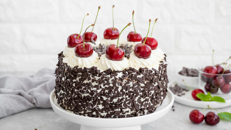Black Forest cake on a white cake stand next to cherries in a bowl