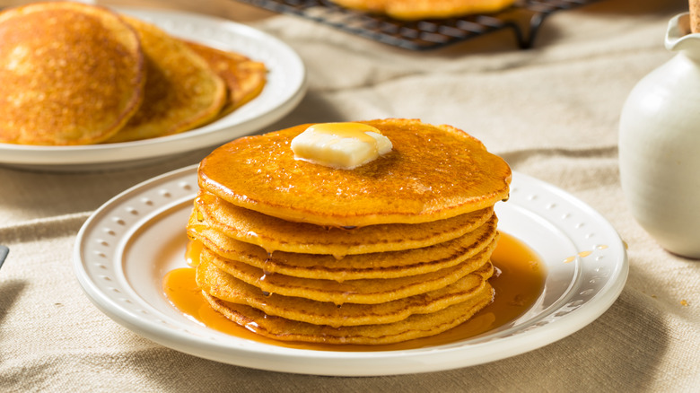 Stack of johnnycakes on a white plate with syrup and butter