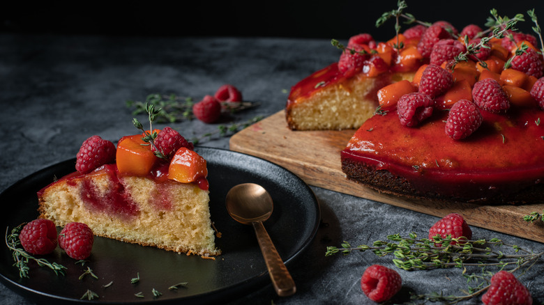 Raspberry poke cake slice on a black plate with a spoon next to the full cake on a wooden board