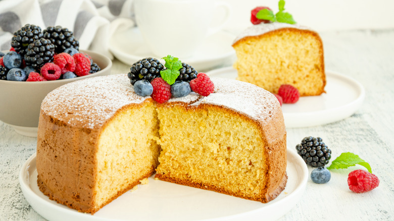Sponge cake and slice on a table with a bowl of fruit