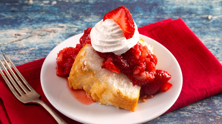 Strawberry shortcake slice on a white plate with a fork and red napkin