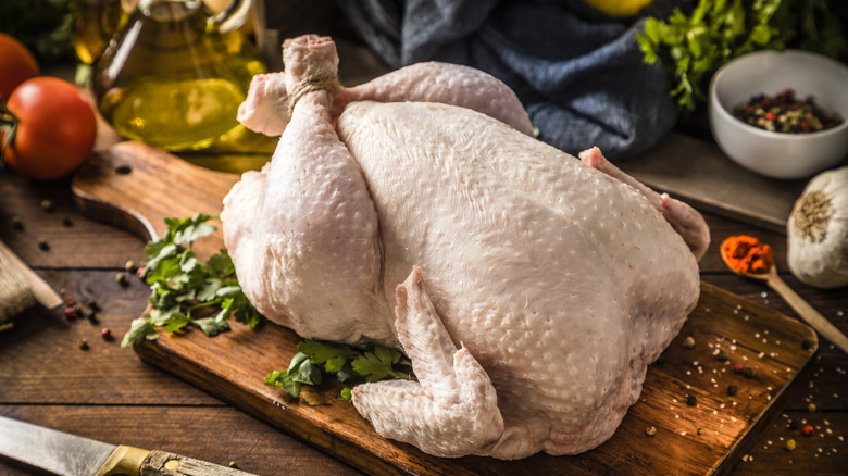 Whole chicken with herbs and spices on a wooden cutting board