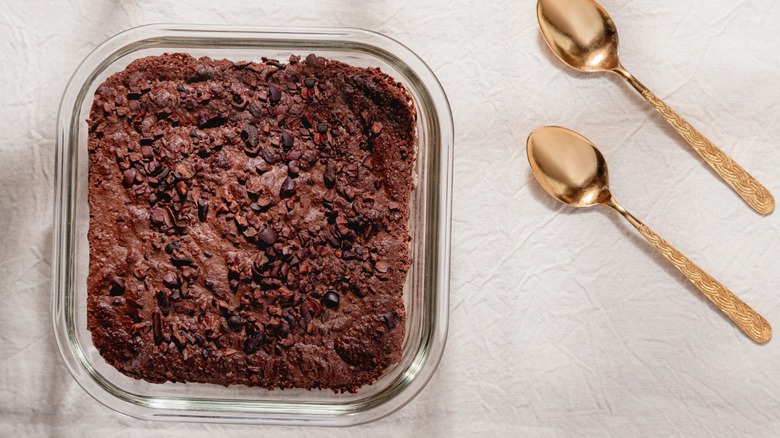 Brownies in a square glass baking dish on a table next to two Golden Spoons