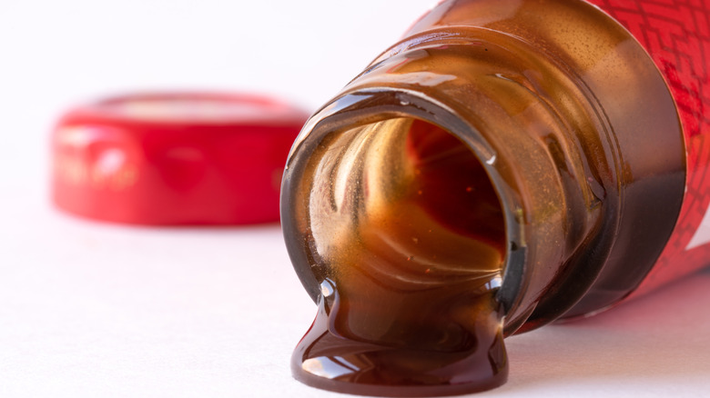 Open bottle of oyster sauce laying down with sauce pouring out