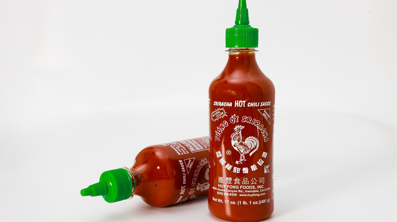 Two bottles of red sriracha sauce with green nozzles