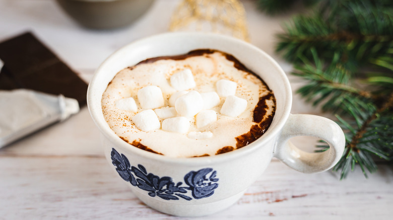 Hot chocolate with whipped cream and marshmallows in white cup with blue flowers