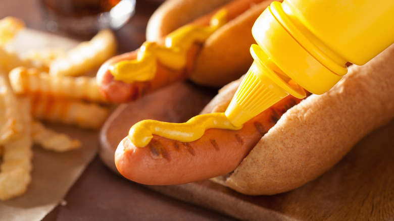 Bottle of mustard squeezing onto hot dog