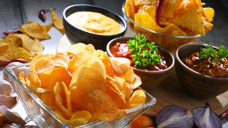 Glass bowls of chips on a table with salsas and dips