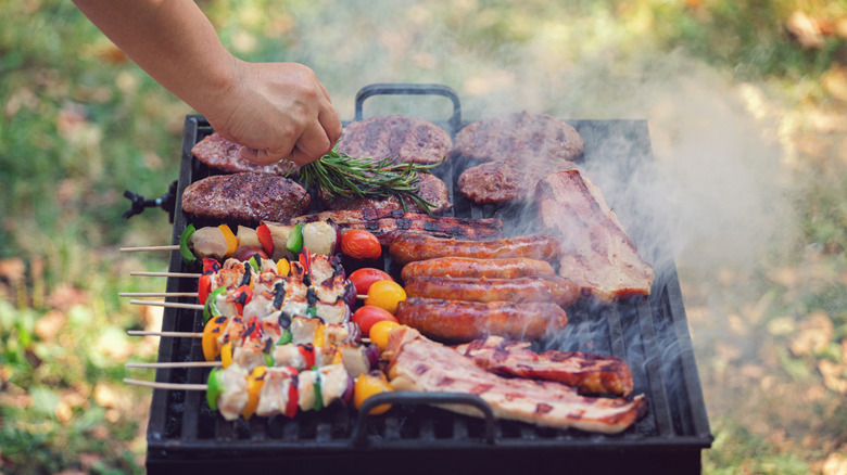 A person grilling burgers, hot dogs, and kebabs on an outdoor barbecue