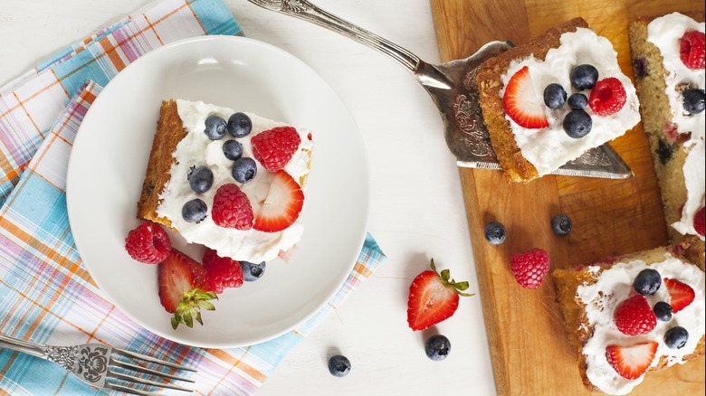 A sheet cake topped in whipped cream, blueberries, and strawberries