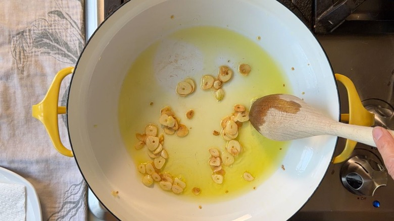 Stirring golden brown garlic chips and olive oil in Dutch oven with wooden spoon.