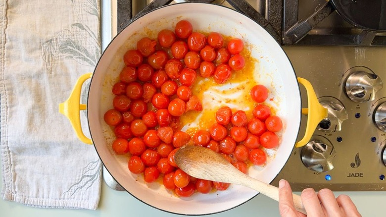 Stirring blistered tomatoes in Dutch oven with wooden spoon on stovetop