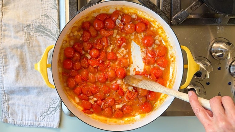 Stirring blistered cherry tomatoes and chopped shallots with wooden spoon on stovetop