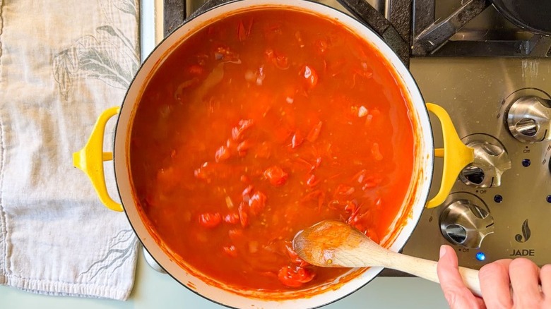 Stirring vegetable stock into cooked tomatoes and shallots in Dutch oven with wooden spoon