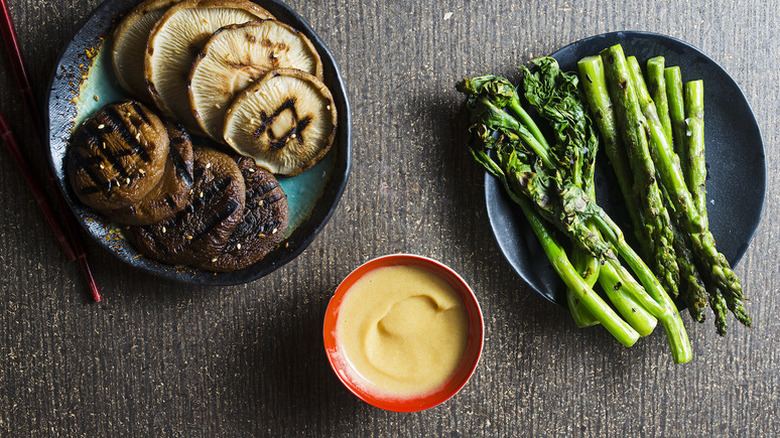 Grilled mushrooms, broccoli, and asparagus on plates next to bowl of creamy miso sauce