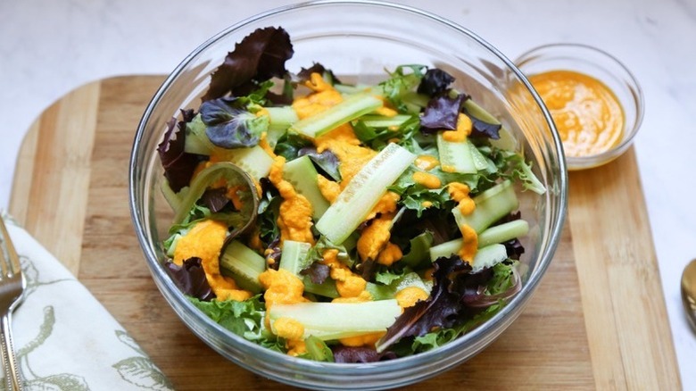 Leafy green and cucumber salad in glass bowl, drizzled with miso ginger dressing