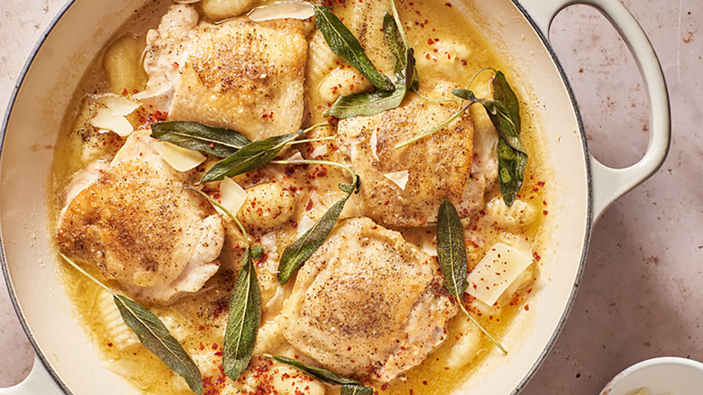 Chicken thighs and gnocchi in casserole pot with buttery sauce and sage leaves