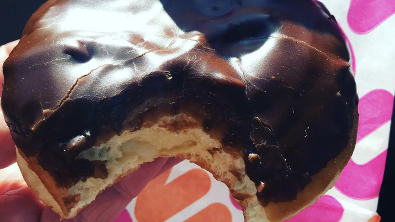 Boston Kreme donut in hand with Dunkin' wrapper