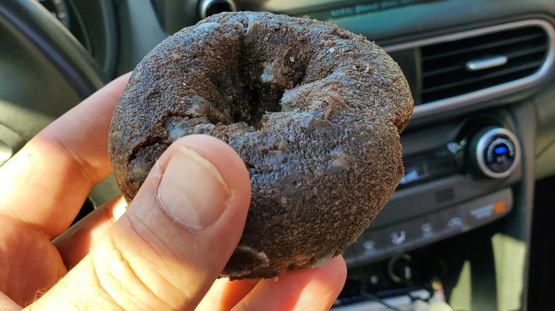 Person holding a chocolate cake donut in a car