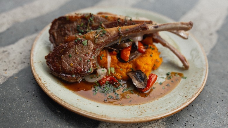 Bone-in lambchops flecked with fresh herbs over a bed of roasted sweet potatoes with onions and red peppers in a pool of juices