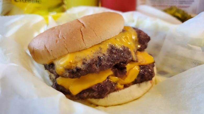 Juicy double cheeseburger with top bun askew sitting on white wax paper