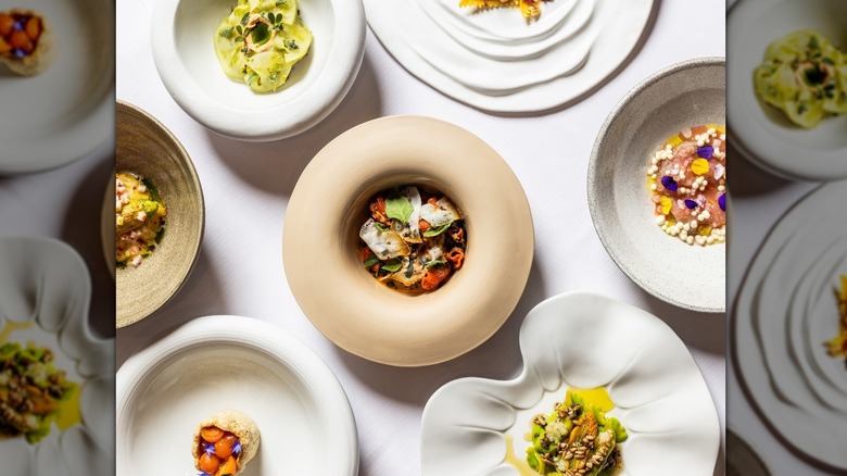 Elegant small white plates of food on white table, with colorful dishes filled with vibrant ingredients and delicate garnishes