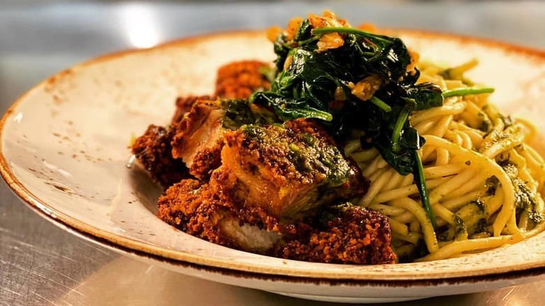 Togarashi-dusted chicken over bed of udon noodles, topped with sauteed spinach on a white flecked plate
