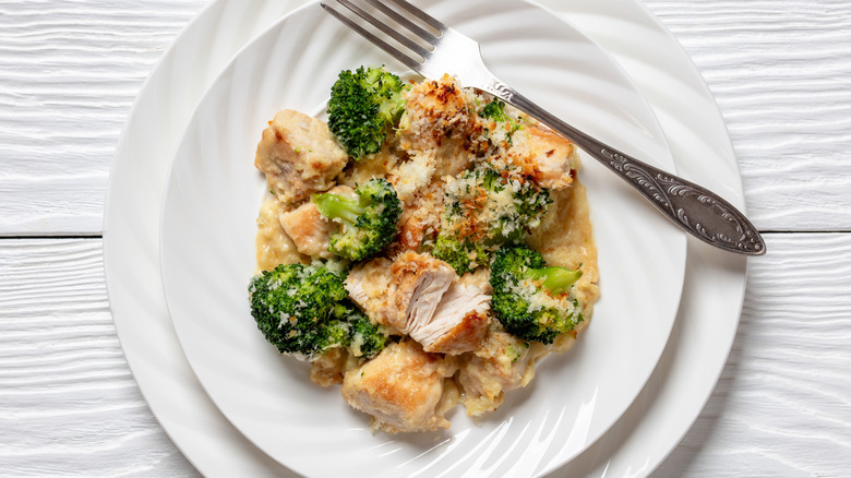 Portion of Chicken Divan on white plate with fork on white wooden table