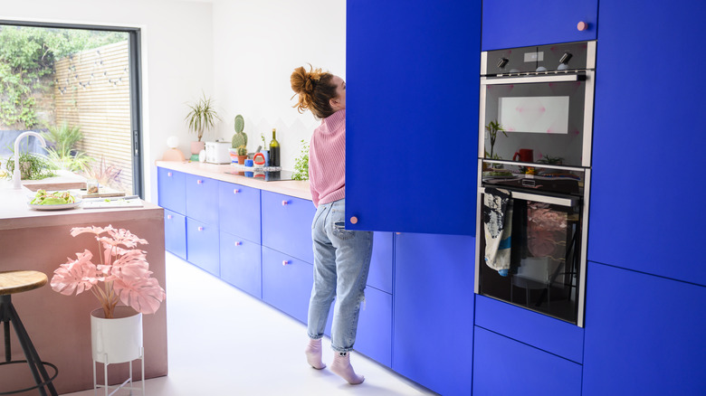 Woman standing in kitchen with electric blue cabinets on the right and a soft pink island on the left