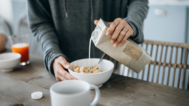 person pouring milk into bowl of cereal