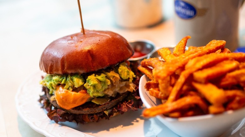 Burger with cheese and avocado alongside a bowl of fries on a white plate