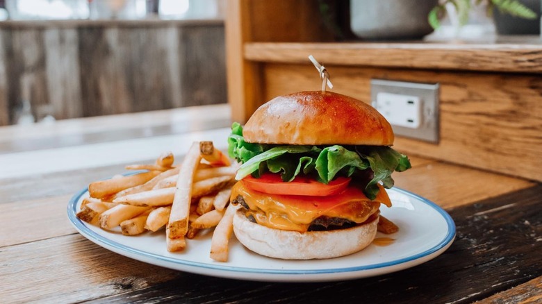 Burger with lettuce, tomato, and cheese on a plate with fries
