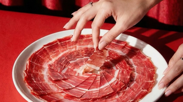 Hand choosing a piece of Ibérico ham from a plate
