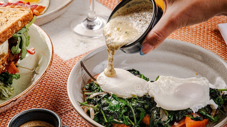 Hand pouring gravy over an egg and vegetable dish
