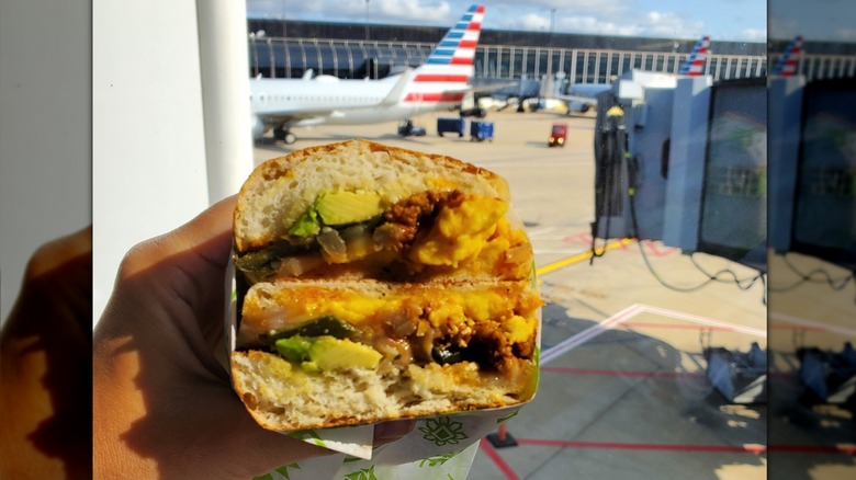 Hand holding a torta in front of an airport window with a view of several airplanes