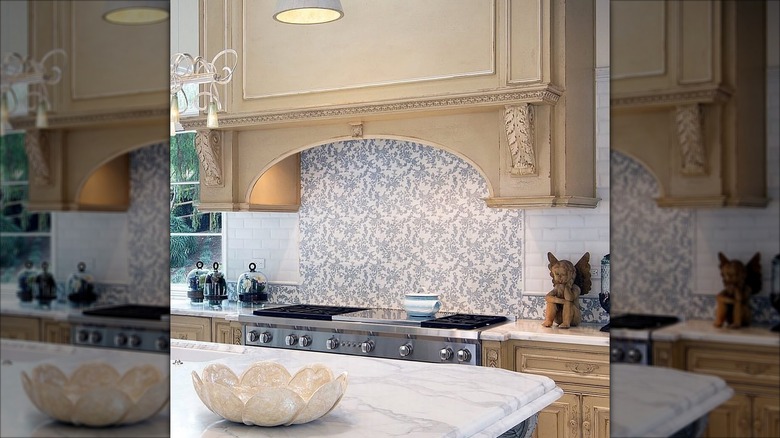 Kitchen with marble countertops, blue floral backsplash and a large beige range hood.