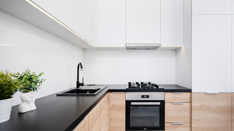 Modern kitchen with white backsplash and upper cabinets, black countertops, and wooden lower cabinets